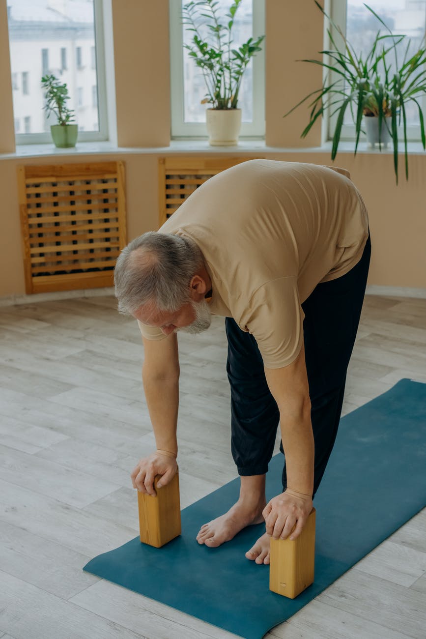 a man in brown t shirt and black pants bending forward pressing on yoga blocks