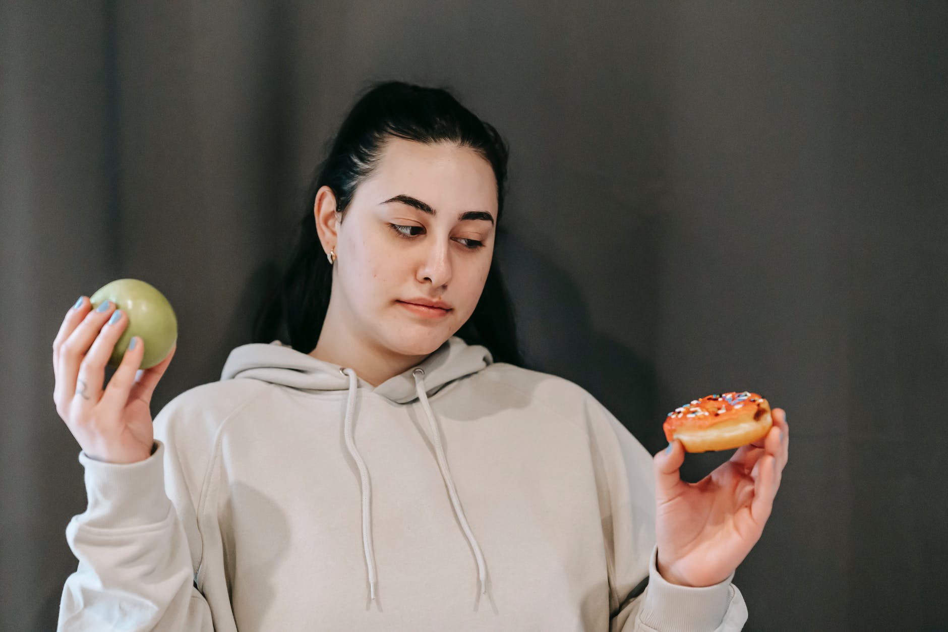 thoughtful woman choosing between green apple and sweet donut