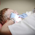 dentist woman wearing white gloves and white scrubsuit checking boy s teeth
