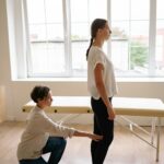 woman in white dress up shirt touching the back of knees of woman in white t shirt