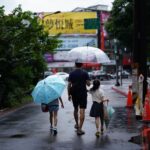 man in blue shirt holding umbrella walking on the street with his kids