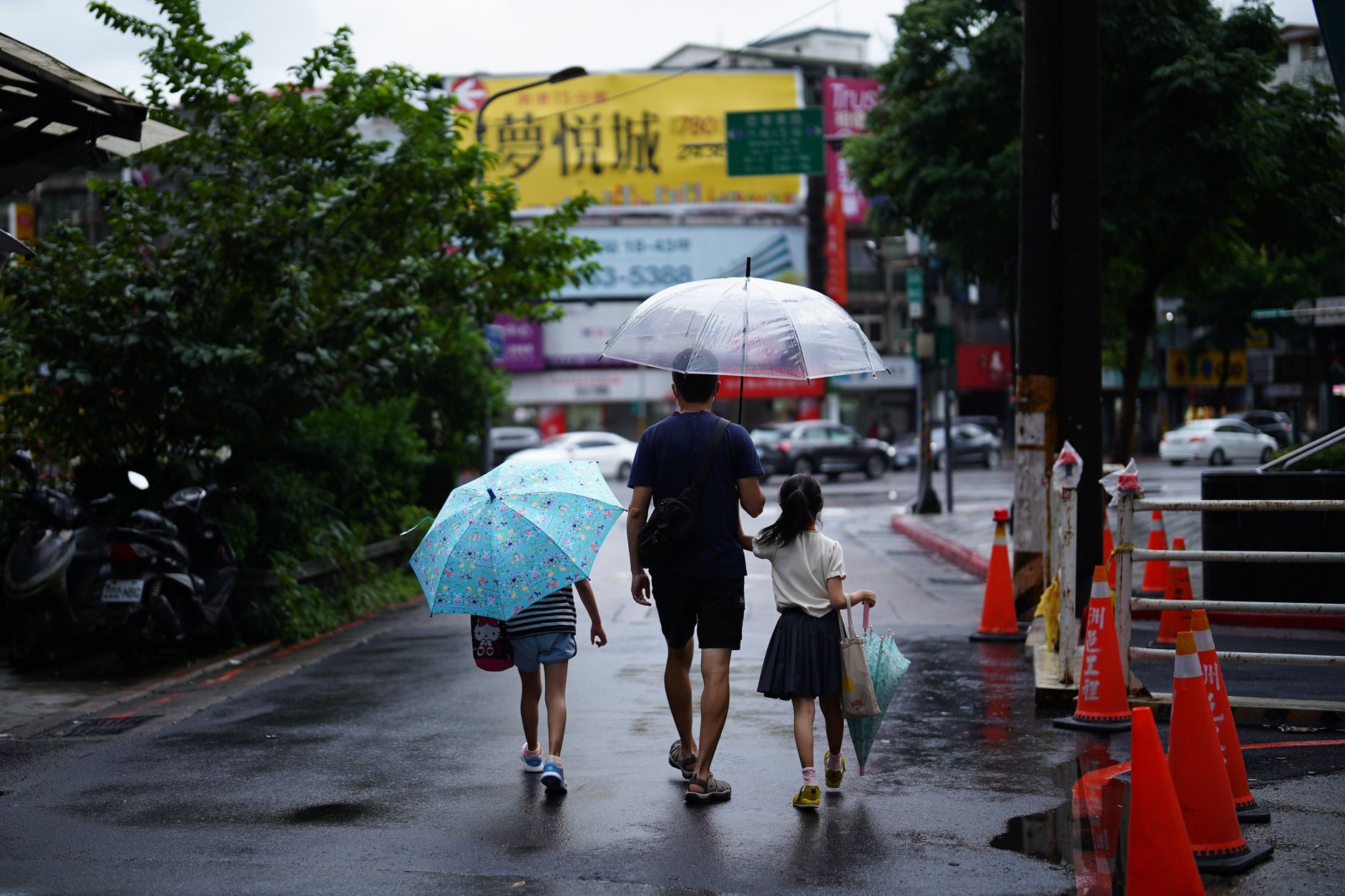man in blue shirt holding umbrella walking on the street with his kids